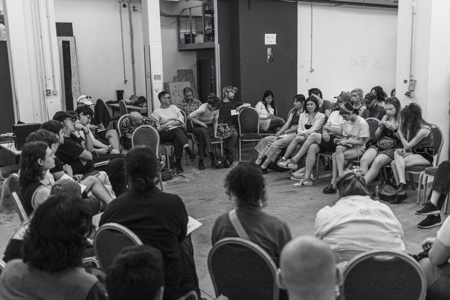 Carnobiała fotografia przedstawiająca uczestników wydarzenia "Post Visual Agreements", grupa osób studenckich w sali siedzących na krzesłach ustawionych w kole