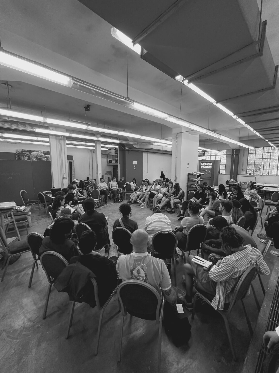 Carnobiała fotografia przedstawiająca uczestników wydarzenia "Post Visual Agreements", grupa osób studenckich w sali siedzących na krzesłach