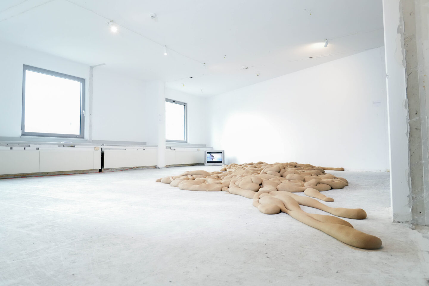 Instalacja stworzona przy pomocy piachu i rajstop, w tle telewizor z projekcją wideo.