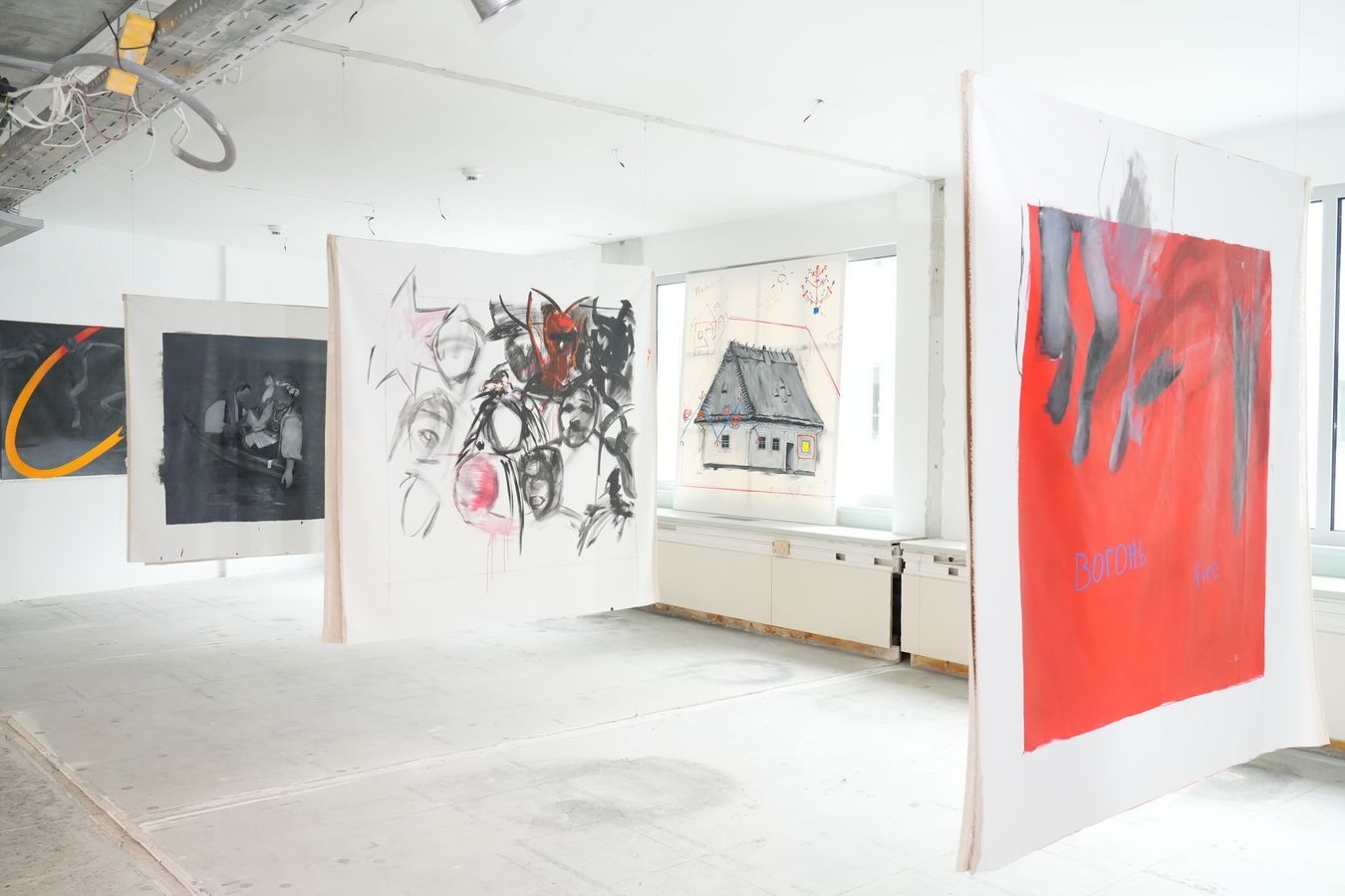 Ekspresyjne prace malarskie wykonane na płótnie, w których dominują odcienie czerni i czerwieni - zawieszone z sufitu, plecami do siebie.