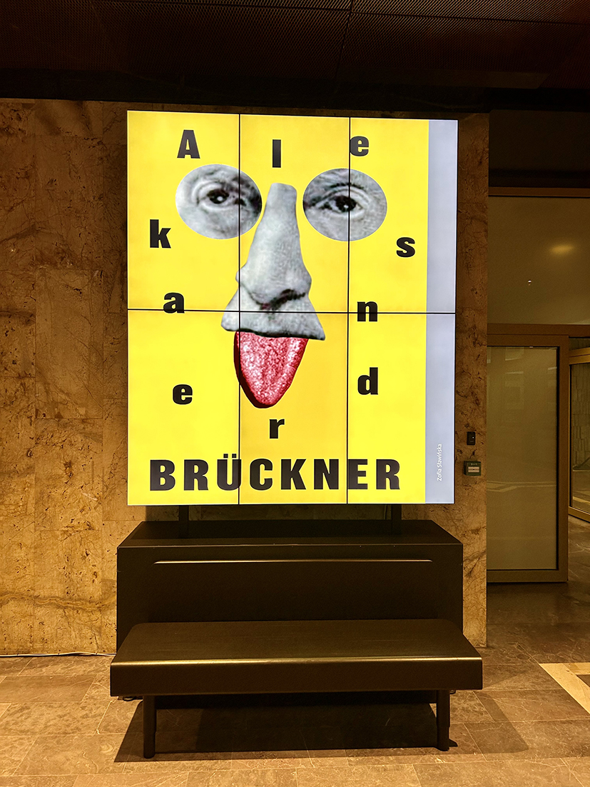 plakat z portretem prof. Aleksandra Brucknera w kolorze żółtym wyświetlony na dużym ekranie w holu Biblioteki Narodowej