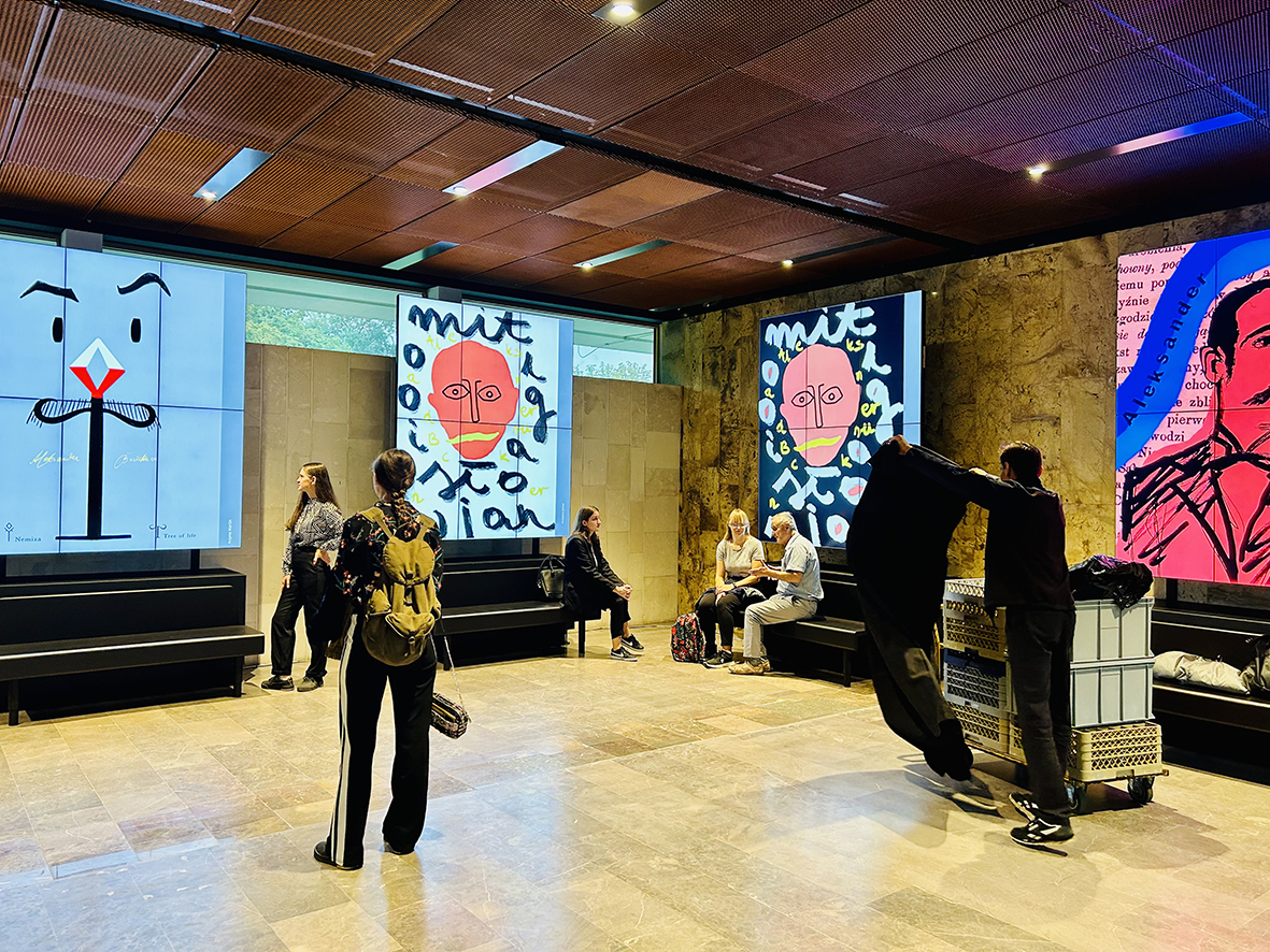 cztery plakaty z portretami prof. Aleksandra Brucknera wyświetlone na dużych ekranach w holu Biblioteki Narodowej