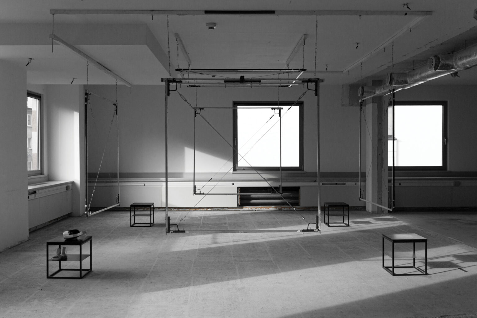 Metalowe obiekty przestrzenne eksponowane w Hop Gallery. Obszar z zaaranżowaną scenografią VR - metalowe, płaszczyzny w formie ram, które nakreślają przestrzeń sześcianu, a w rogach stoliki z okularami do VR.