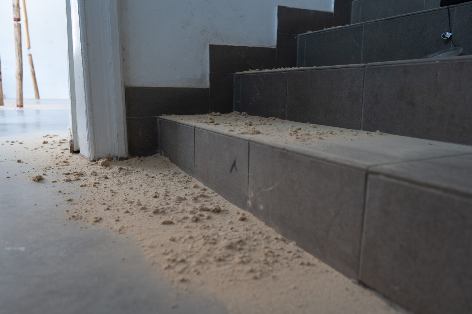 Instalacja przestrzenna składająca się z drewnianych belek rozpostartych pomiedzy sufitem a podłogą. Obok belek pozostałości po leżą wióry, pozostałości po obróbce drewna.