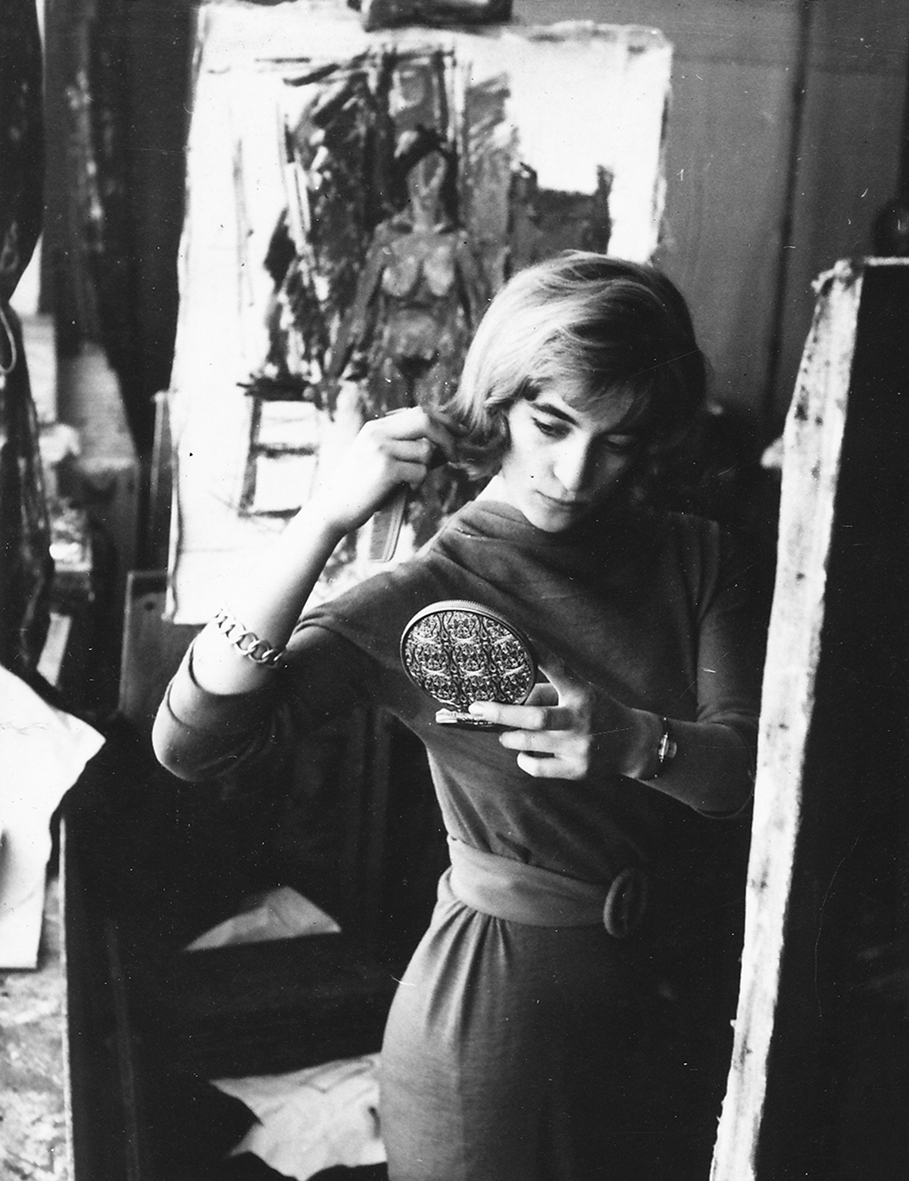 Teresa Wilbik w pracowni malarstwa prof. Eibisha na Wydziale Malarstwa w latach 60-tych XX wieku. Elegancko ubrana kobieta przegląda się w trzymanym w dłoni bogato dekorowanym lustrze.