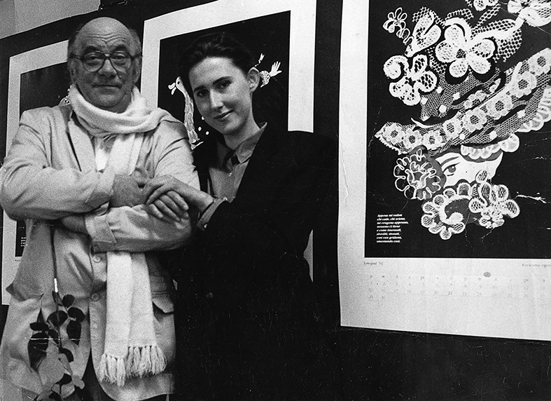 Janusz Stanny z dyplomantką Dorotą Kołodyńską. Czarno białe zdjęcie ukazujące mężczyznę i kobietę trzymających się za ręce. Stoją na tle oprawionych grafik.