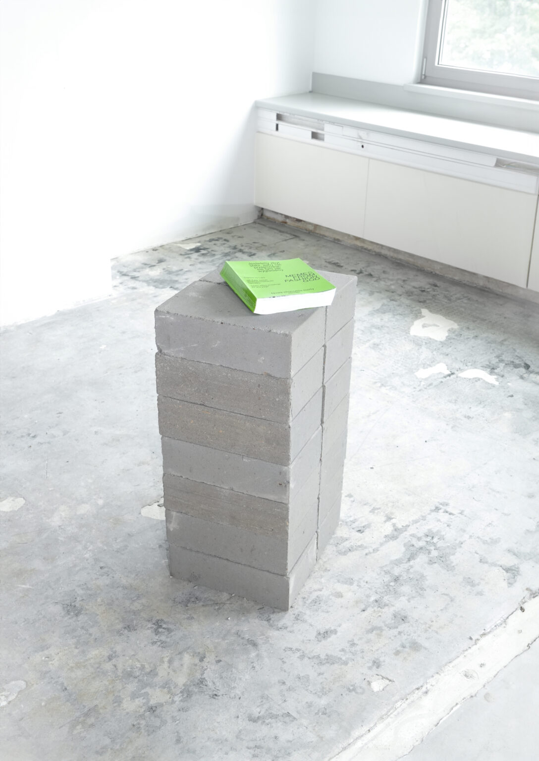 Dokumentacja dyplomu magisterskiego mgr Natalii Parandyk. Zielona książka leżąca na betonowych bloczkach w industrialnej przestrzeni.