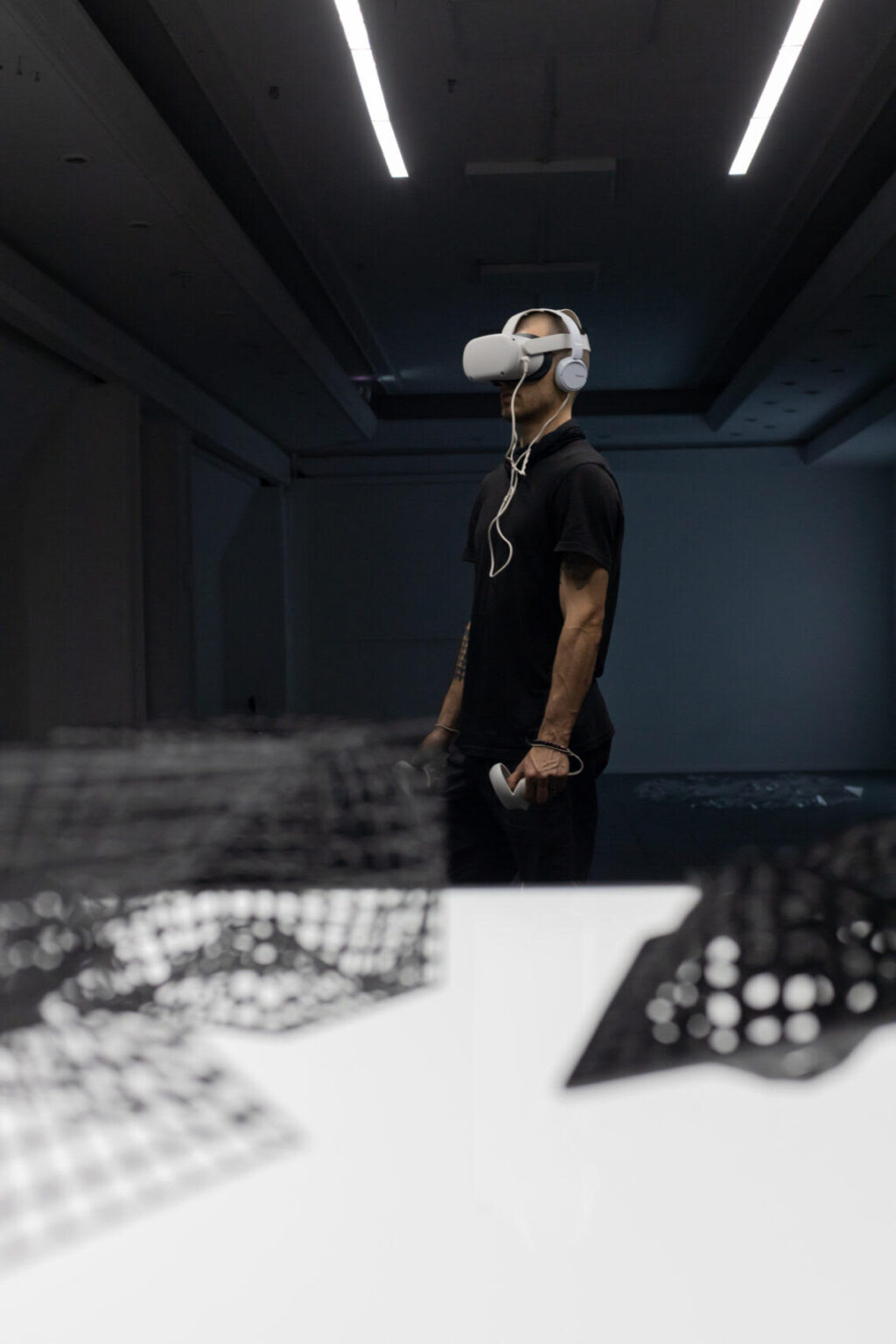 Osoba ubrana na czarno doświadcza pracy dyplomowej Rafała Kruszki w przestrzeni galeryjnej. Na głowie ma założone gogle VR.