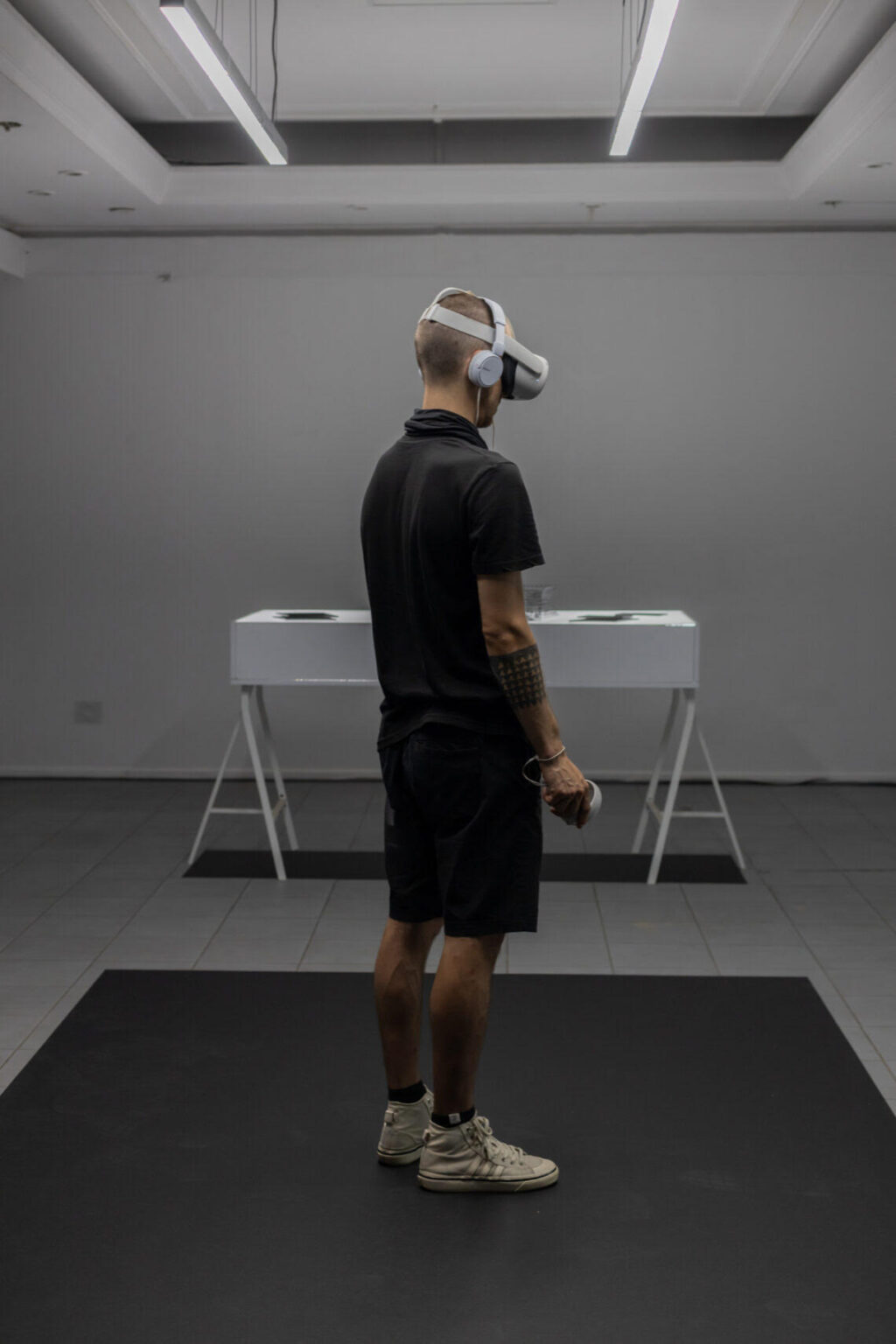 Osoba ubrana na czarno doświadcza pracy dyplomowej Rafała Kruszki w przestrzeni galeryjnej. Na głowie ma założone gogle VR.