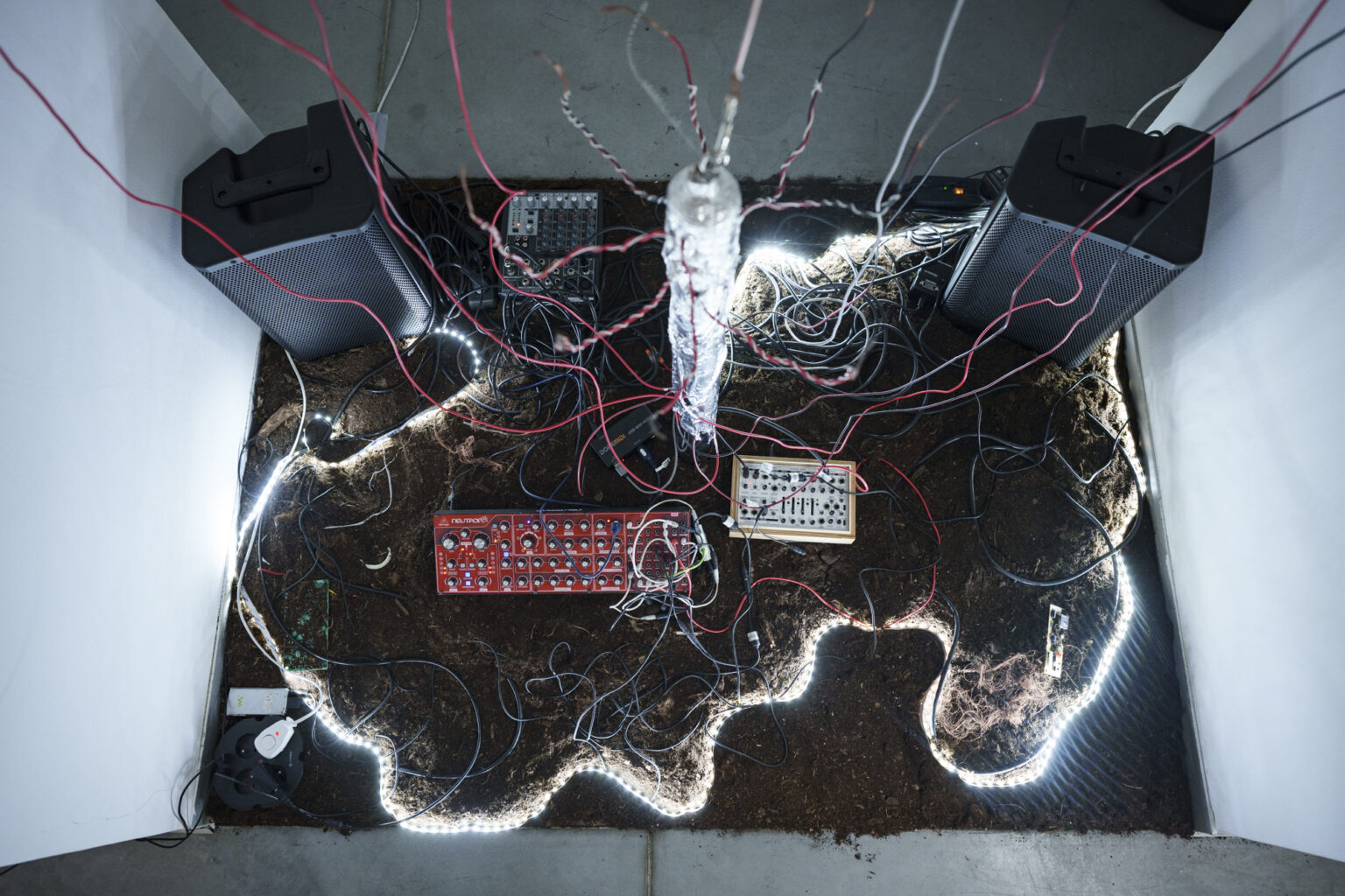 Instalacja z kablami, głośnikami i syntezatorami ułożonymi na ziemi, otoczona świecącymi taśmami