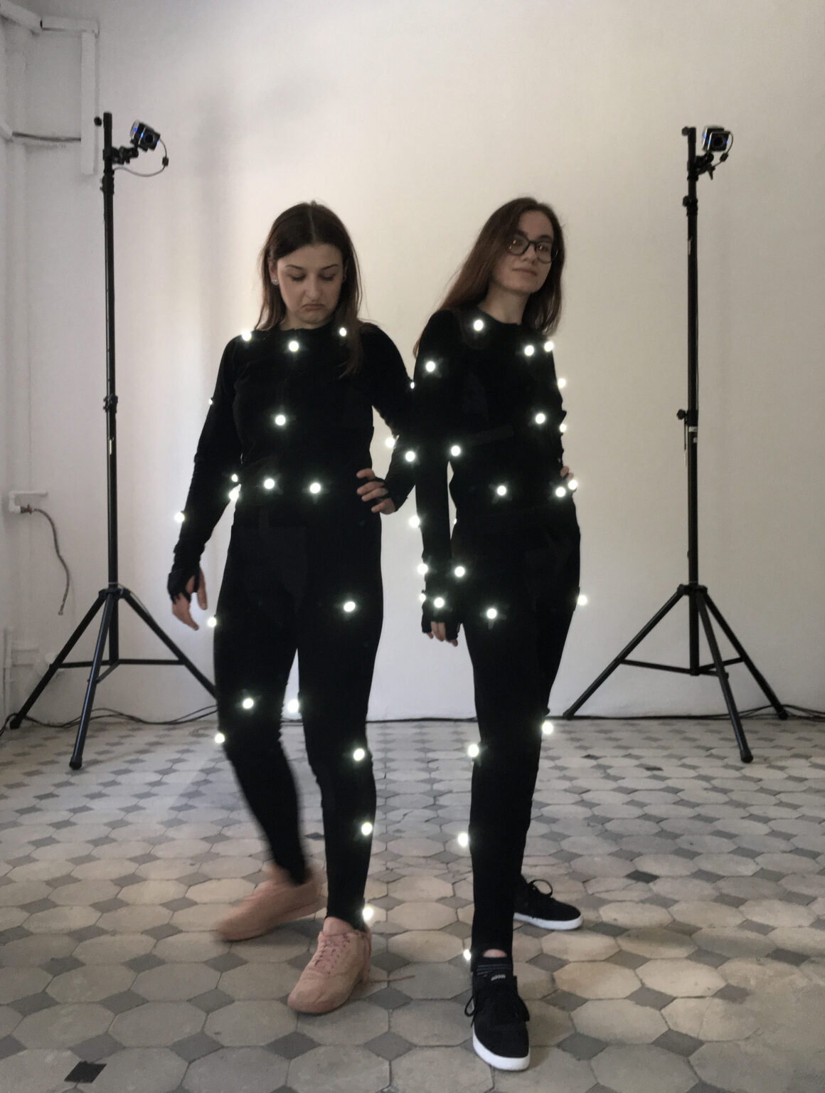2 osoby pozują w strojach do motion capture, wyraźnie świecą się markery do trackowania ruchu.
