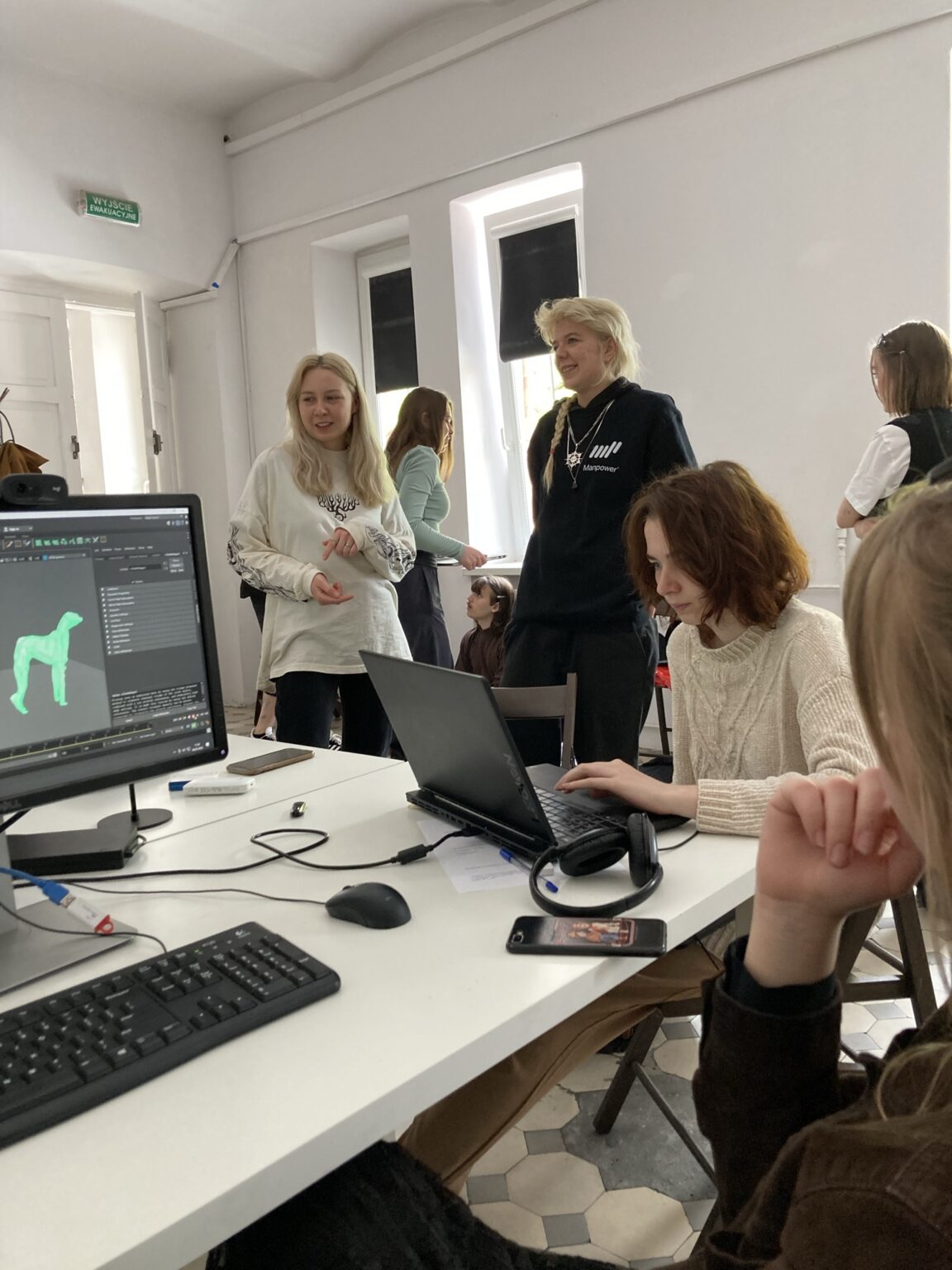 2 osoby siedzą przy komputerze, kilka osób w tle rozmawia.