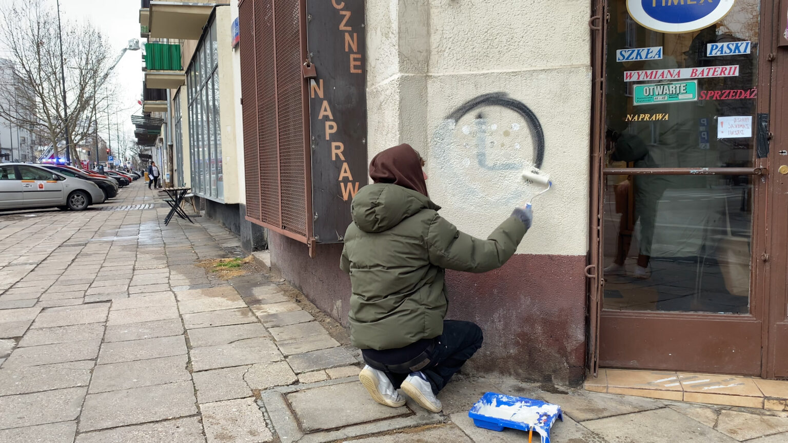 Kadr z filmu. Osoba zamalowuje graffiti na murze.