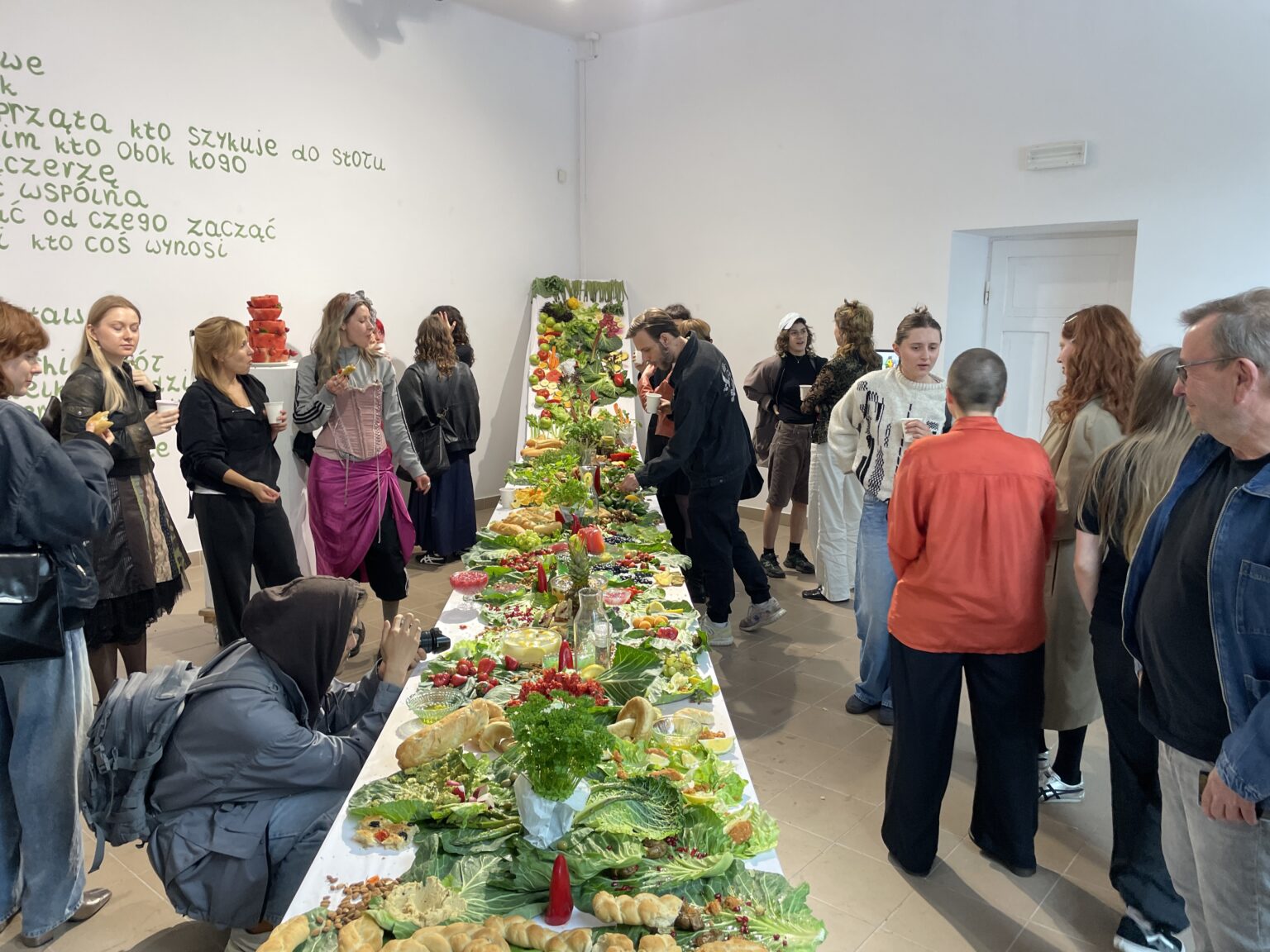 W sali wystawienniczej znajduje się kilkadziesiąt osób. Po środku tej sali ustawiony jest długi stół. Stół jest przykryty białym obrusem a na nim są ułożone potrawy, które przykrywają praktycznie całą powierzchnię stołu. Potrawy ułożone są w różne kształty, mozaikę – tworzą coś w rodzaju abstrakcyjnego obrazu.