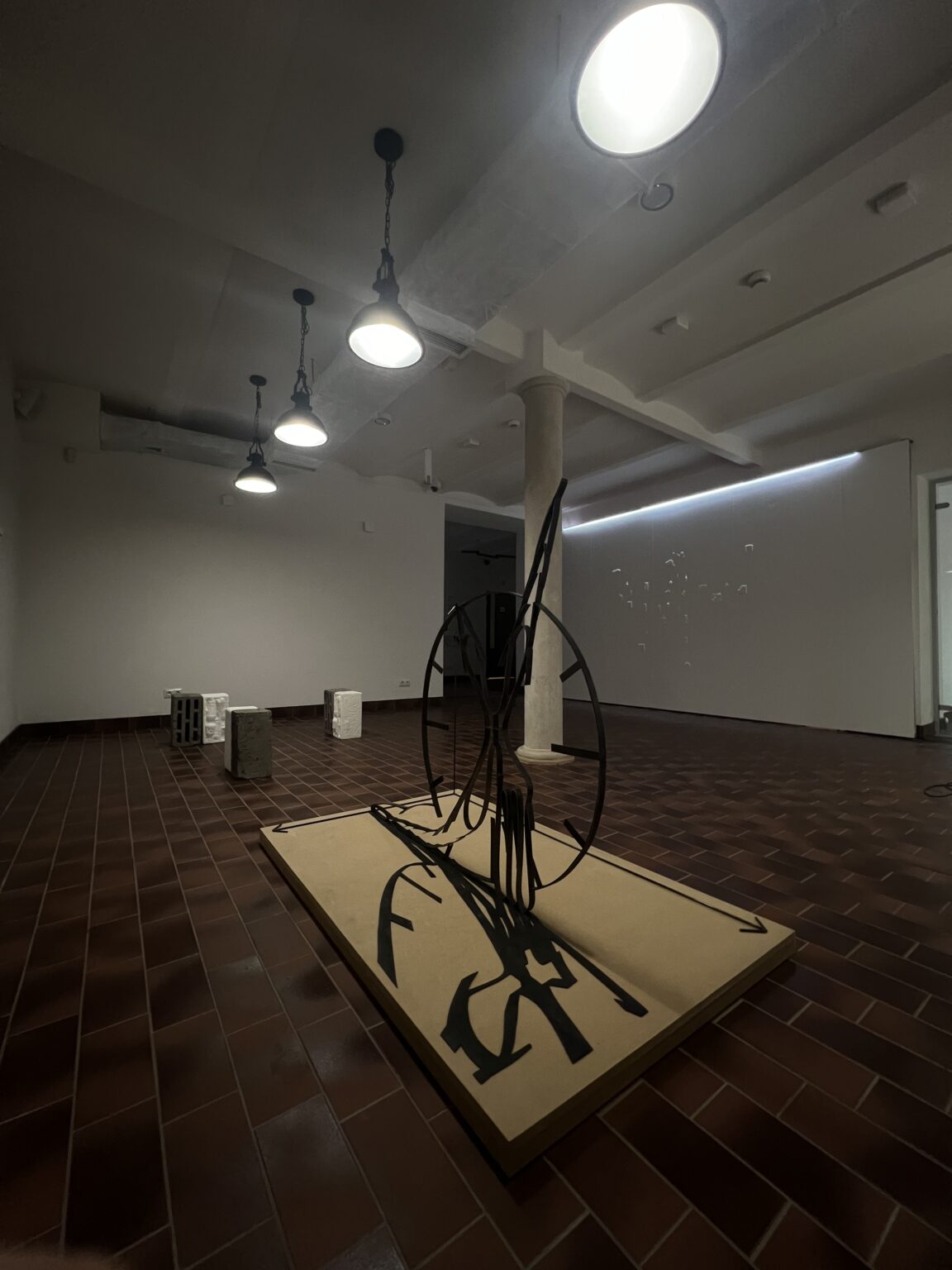 Widok wystawy, szerokokątny kadr. N pierwszym planie obiekt z motywem ażurowego abstrakcyjnego zegara.