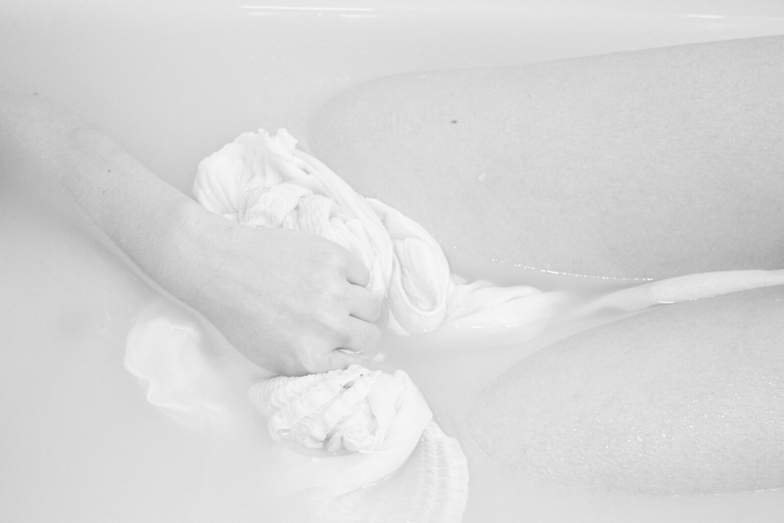 fragment sylwetki zanurzonej w zabielonej wodzie w wannie. Ręka trzyma biały materiał zakrywający krocze.