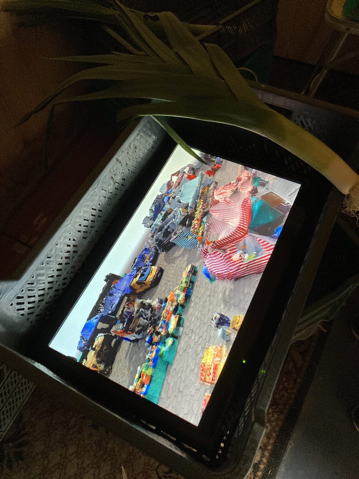 por położony na zielonej plastikowej skrzynce, w skrzynce ekran TV, na ekranie kadr z animacji 3D, z zeskanowanym w technice 3D bazarem.