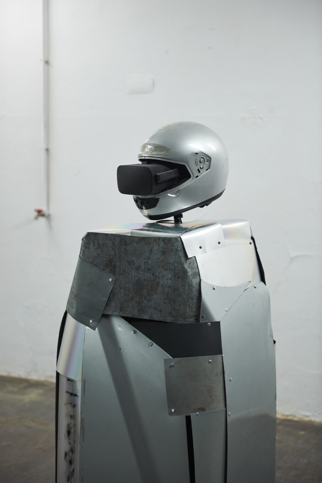 zdjęcie, fragment instalacji. Gogle VR włożone w podniszczony kask od motoru, pod spodem większa część zrobiona z kawałków blachy.