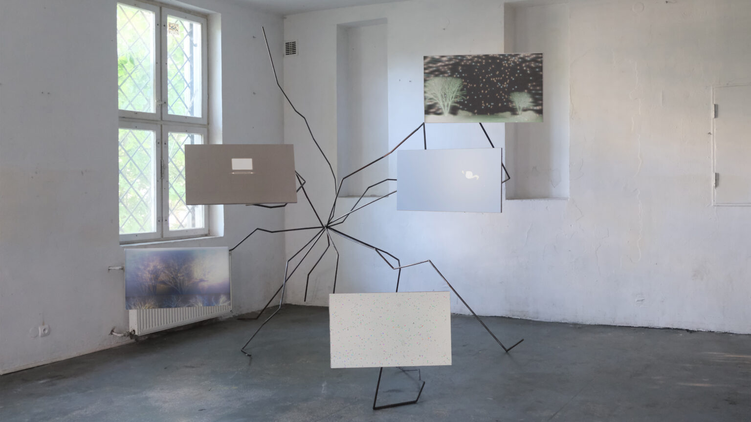 widok wystawy, instalacja. Rozchodzące się z jednego punktu stalowe pręty, powyginane i spawane tak, że tworzą krótsze proste odcinki. Na końcach pięciu prętów przytwierdzone są styrodurowe prostopadłościany. Prostopadłościany przypominają ekrany, projektowane są na nie animacje, głównie 3D. Delikatne, nostalgiczne, momentami nieostre.